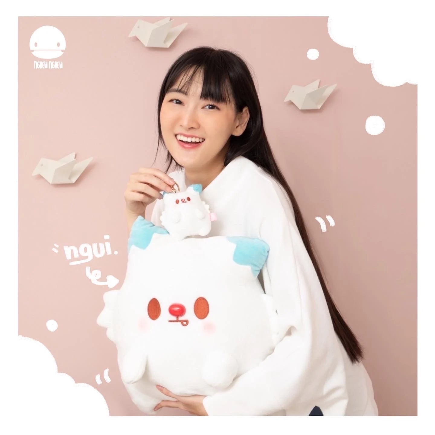 Young woman holding Ngaew Ngaew Plush and a matching keychain, both cat-like, with blue ears and rosy cheeks, embodying Strangecat Toys' quirky art toy style.