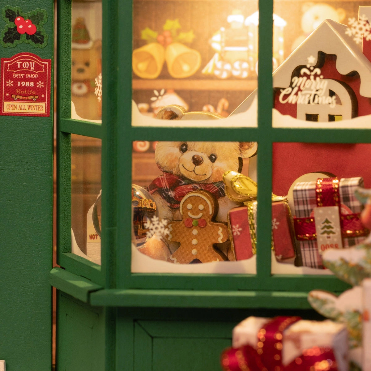 Rolife 3D Wooden Puzzle - Santa's Toy Shop DP006 features a festive toy shop scene with a teddy bear, gingerbread ornament, and holiday decorations viewed through a window.