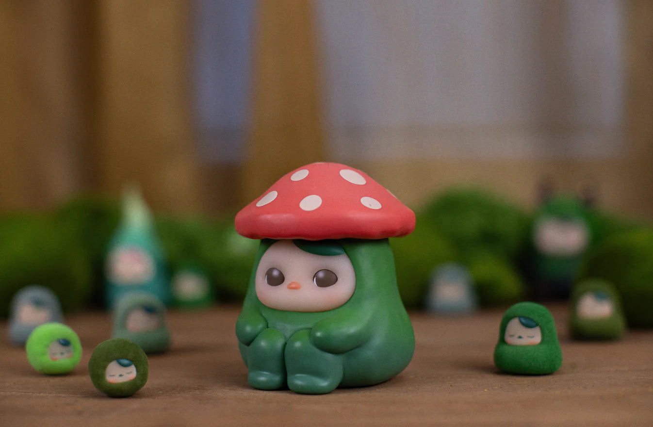 Red Poka Mushroom B by Pucky: A whimsical vinyl figure with a red mushroom cap, surrounded by smaller green versions on a wooden tabletop.