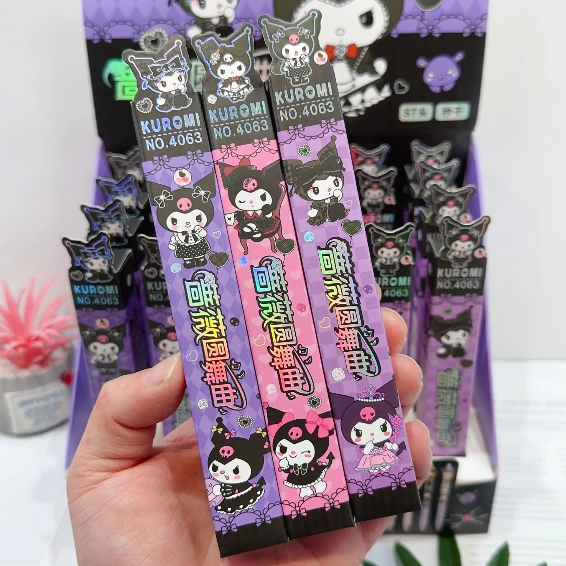 A hand holding a Kuromi - Waltz of the Roses blind box pen, surrounded by colorful candy and cartoon character boxes, embodying Strangecat Toys' blind box and art toy store essence.