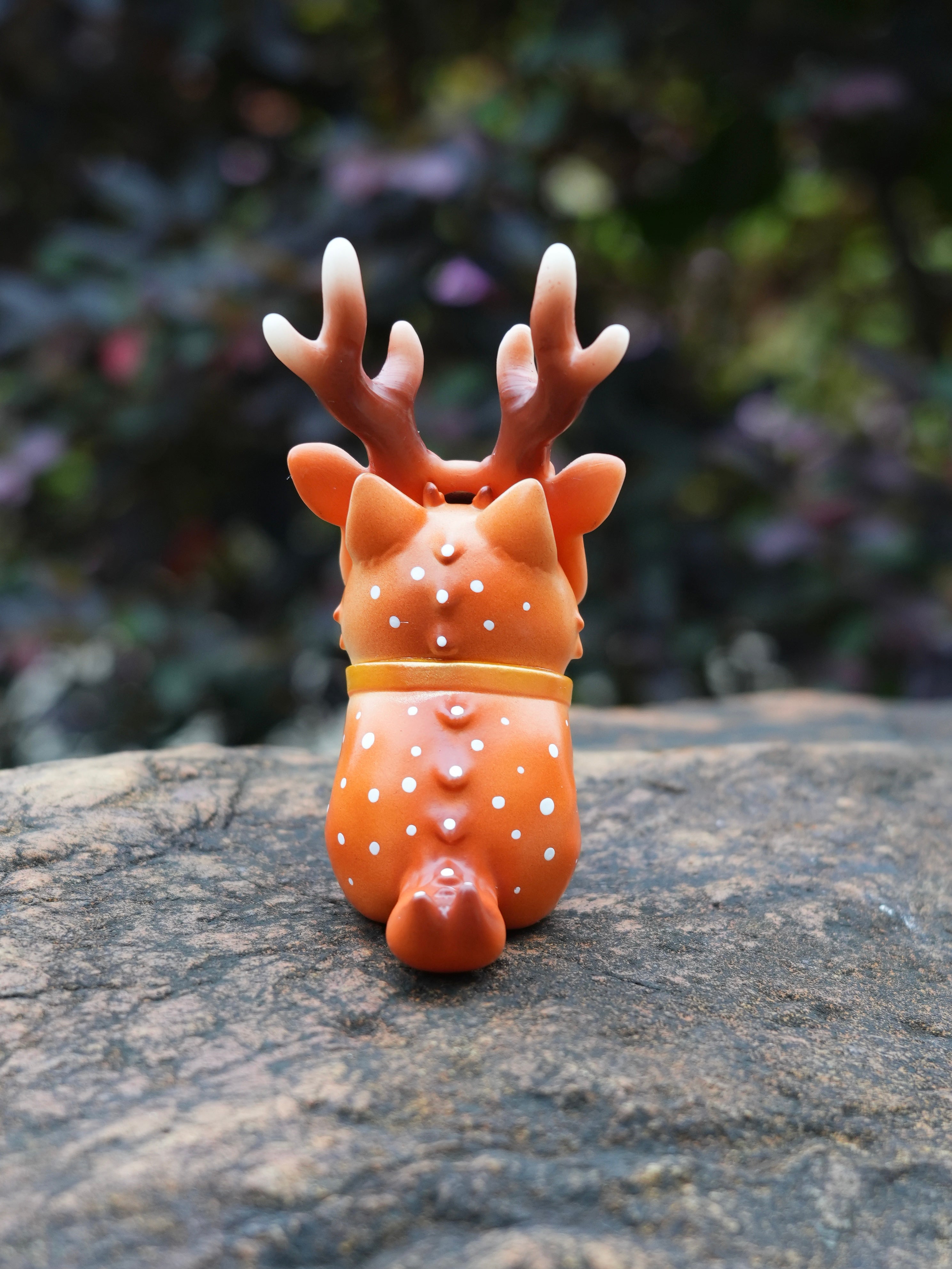 Spotted Deer Cat by HOTRU, a small, orange vinyl figurine with white spots and cream-tipped antlers, sitting outdoors on a rock.