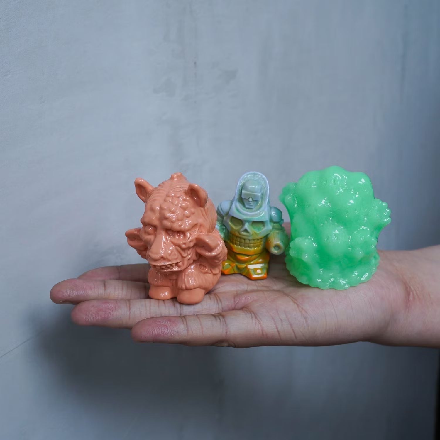 Hand holding three Retroband & Zectron Presents WHO GOES THERE? VERSUS Blind Box mini figures: horned ogre, hooded skeleton, and glossy slime creature, showcasing diverse toy designs.