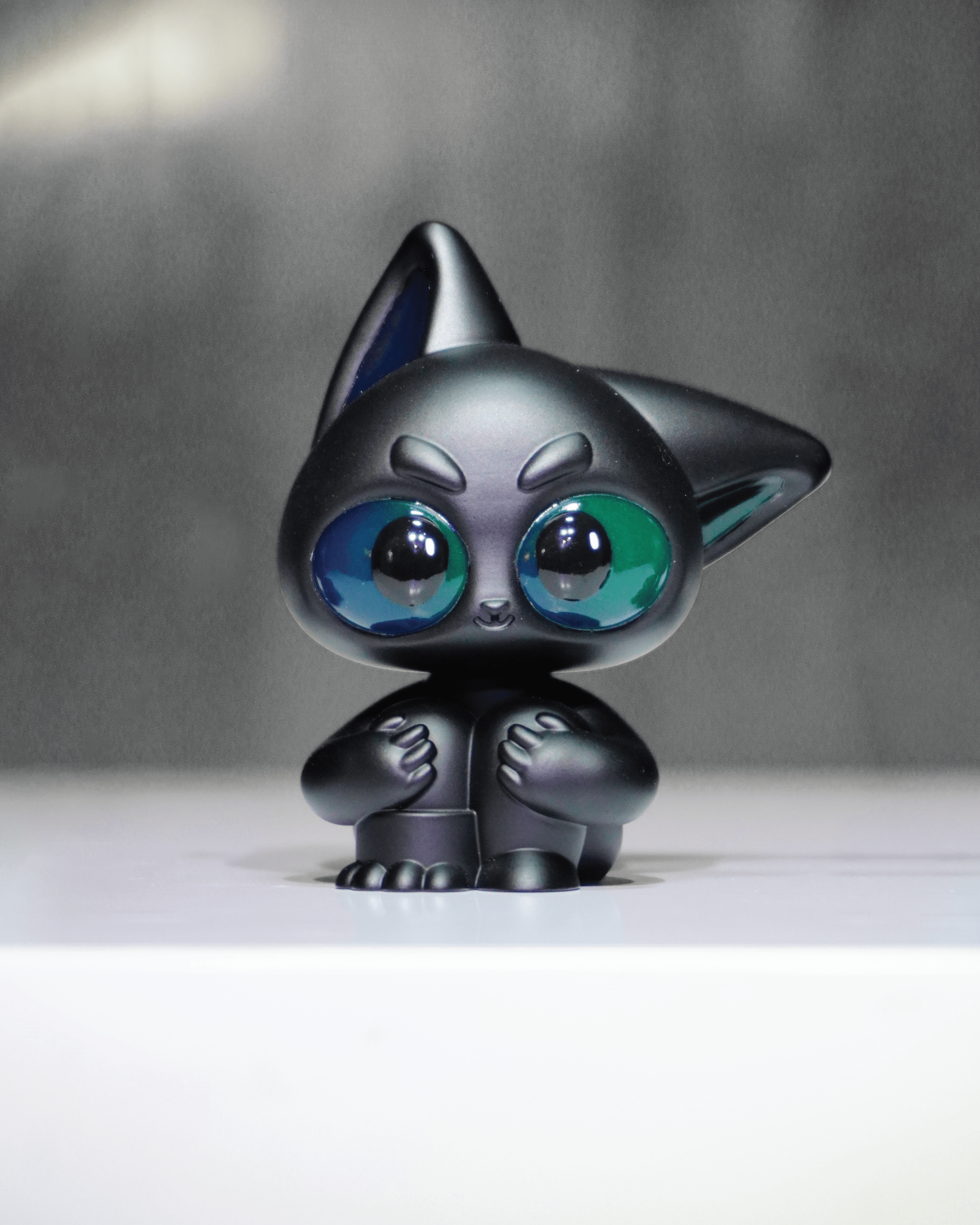 Noir by Wapu: A matte-black, stylized resin figurine with green-blue eyes, pointed ears, and small paws, embodying a cat or fox-like creature.