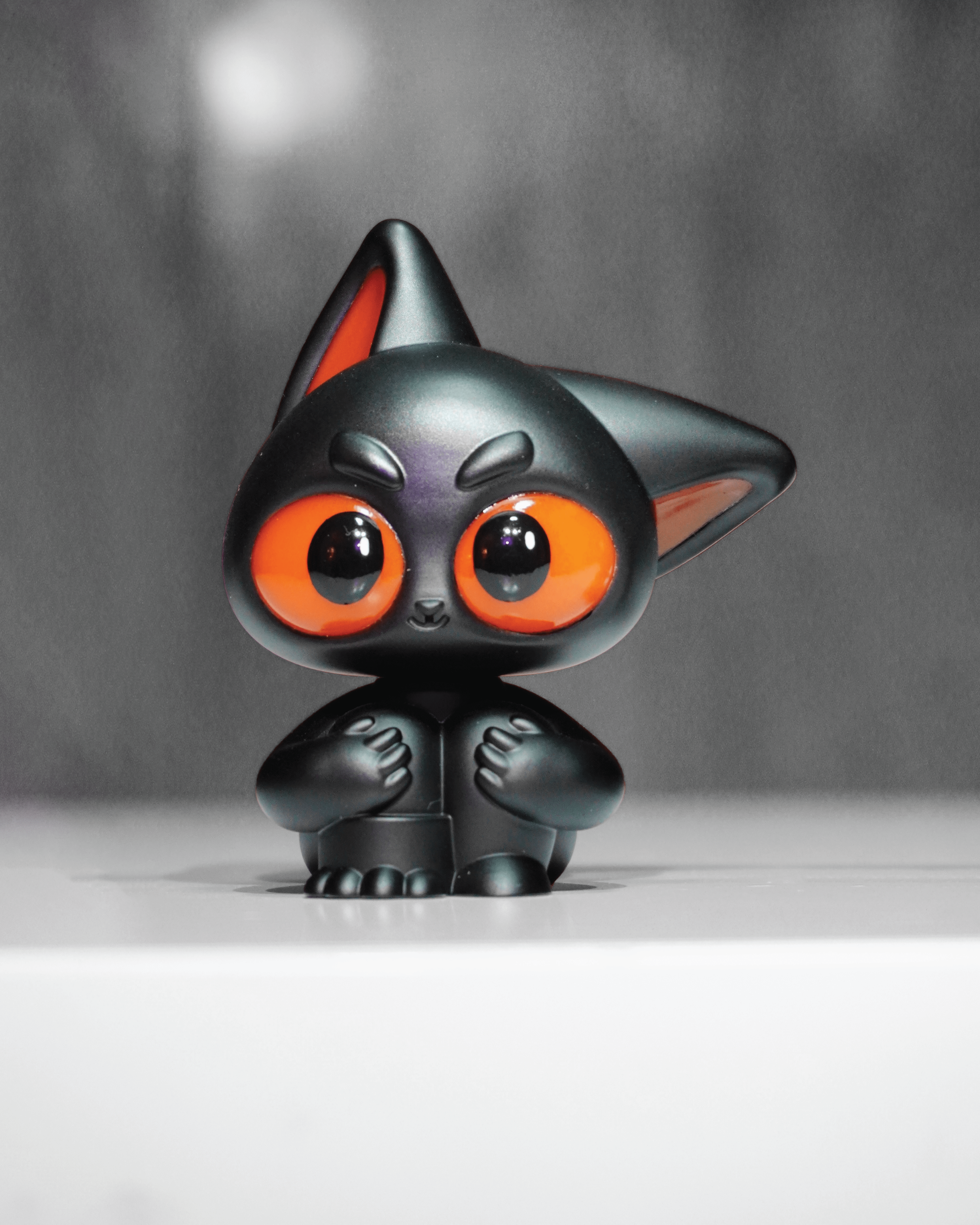 Noir by Wapu, a matte black designer toy cat figurine with glossy orange eyes and a rounded body, sits on a white surface.
