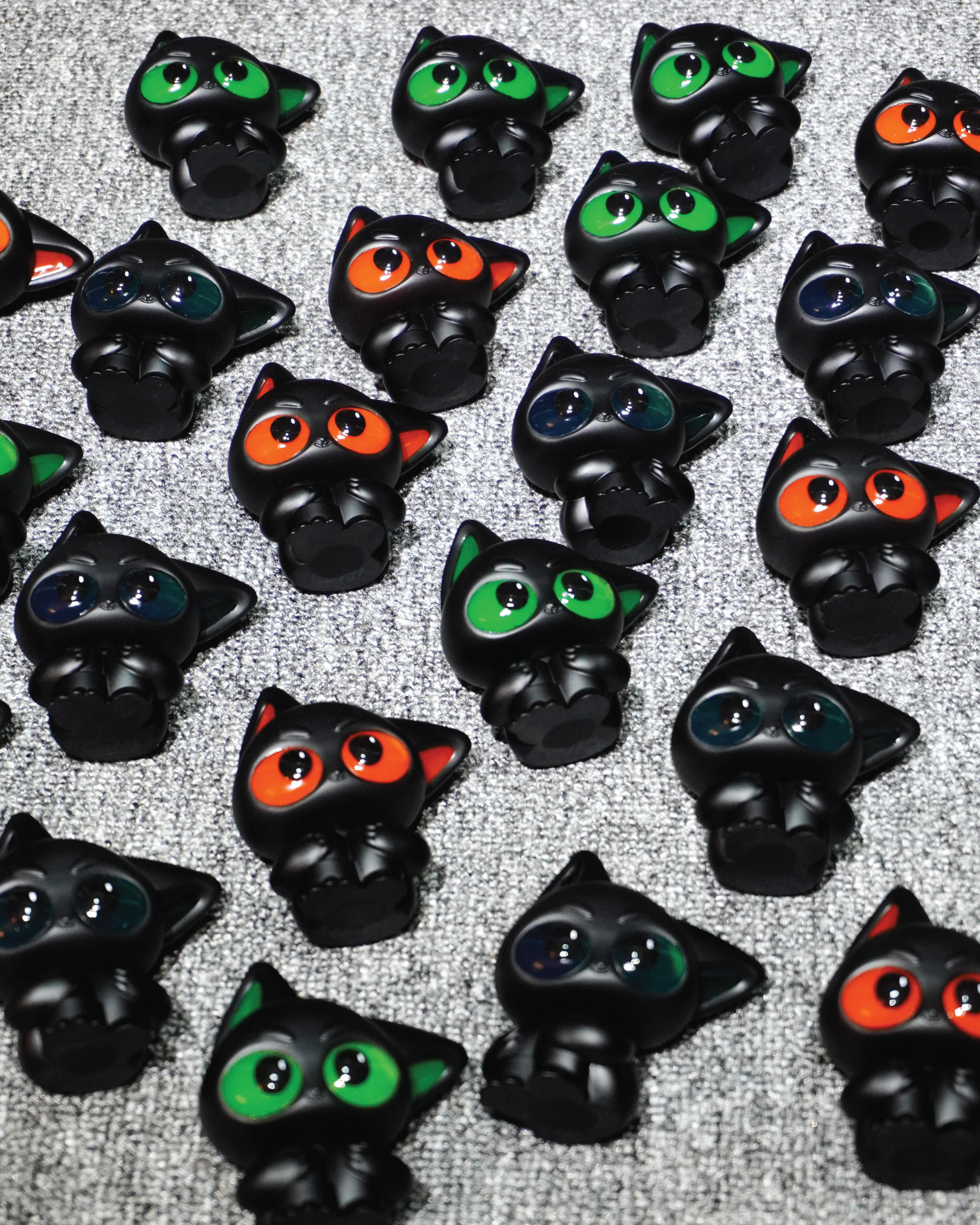 Noir by Wapu: Stylized black cat keycaps with glossy, multicolored eyes, arranged on a grey surface, embodying Strangecat Toys' unique art toy collection.