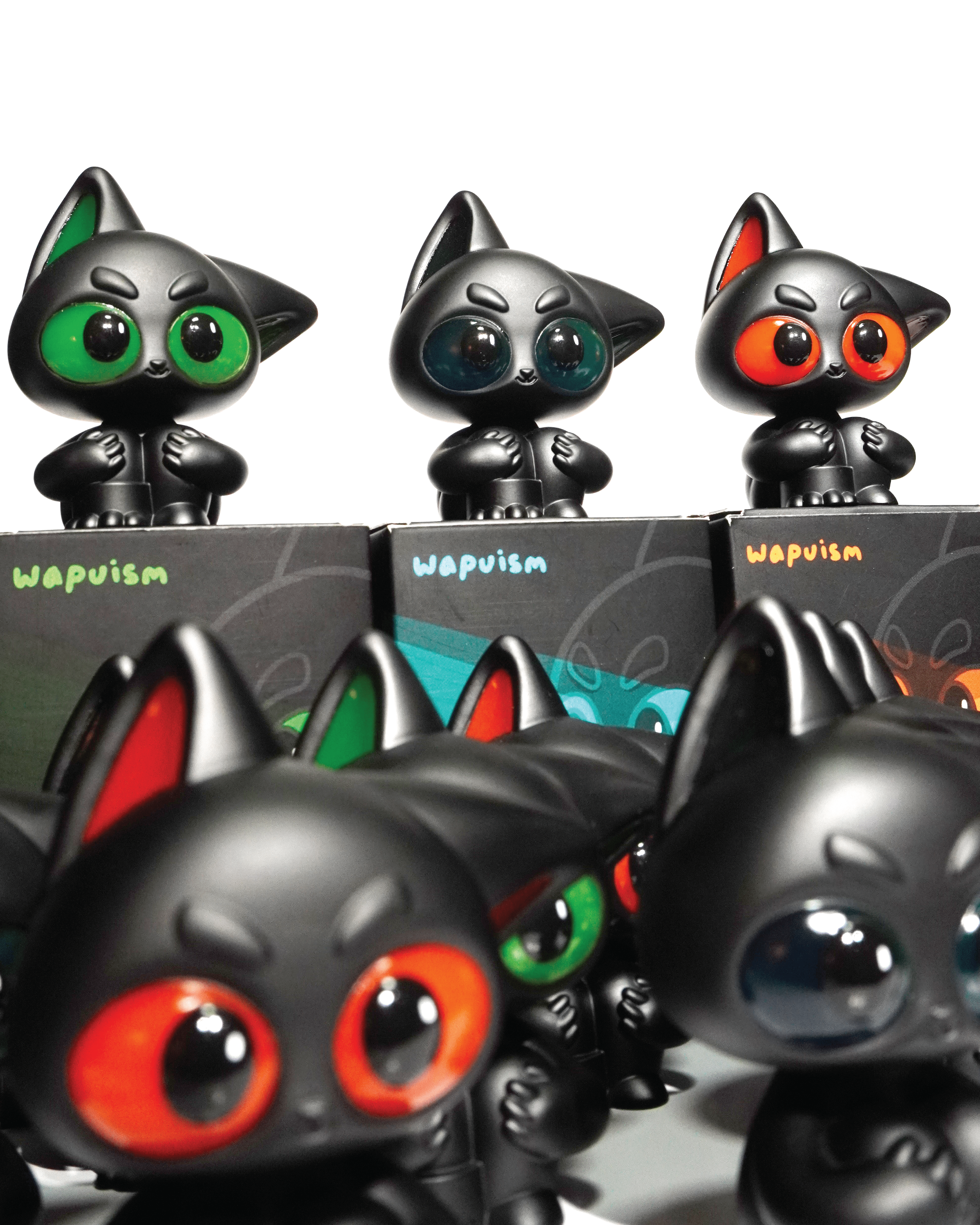 Noir by Wapu: matte black vinyl cat figurines with glossy eyes in green, blue, or orange, arranged on Wapuism boxes.