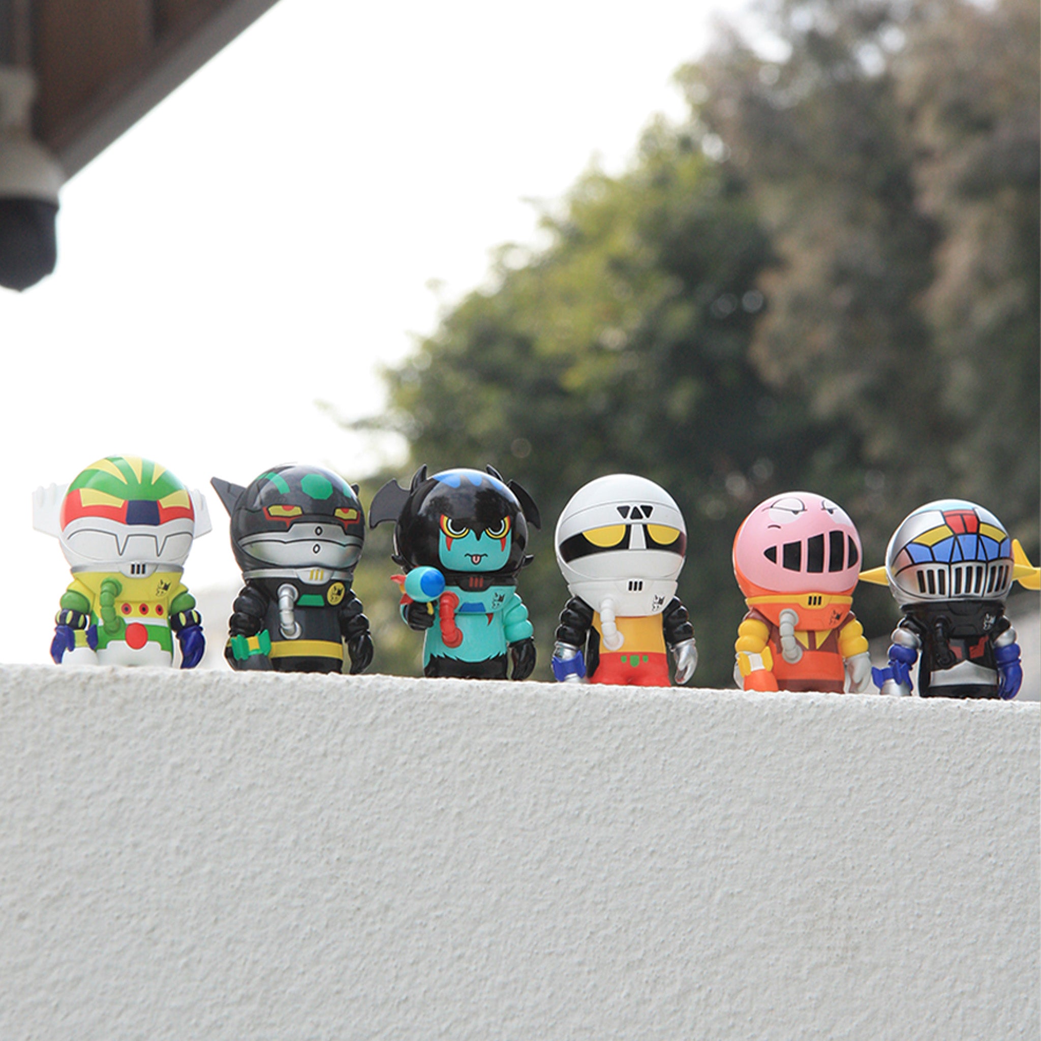 SAMSAM ADVENTURER X GO NAGAI BLIND BOX figures, featuring six unique vinyl designs, displayed outdoors on a ledge. Part of a collectible series, ideal for art toy enthusiasts.