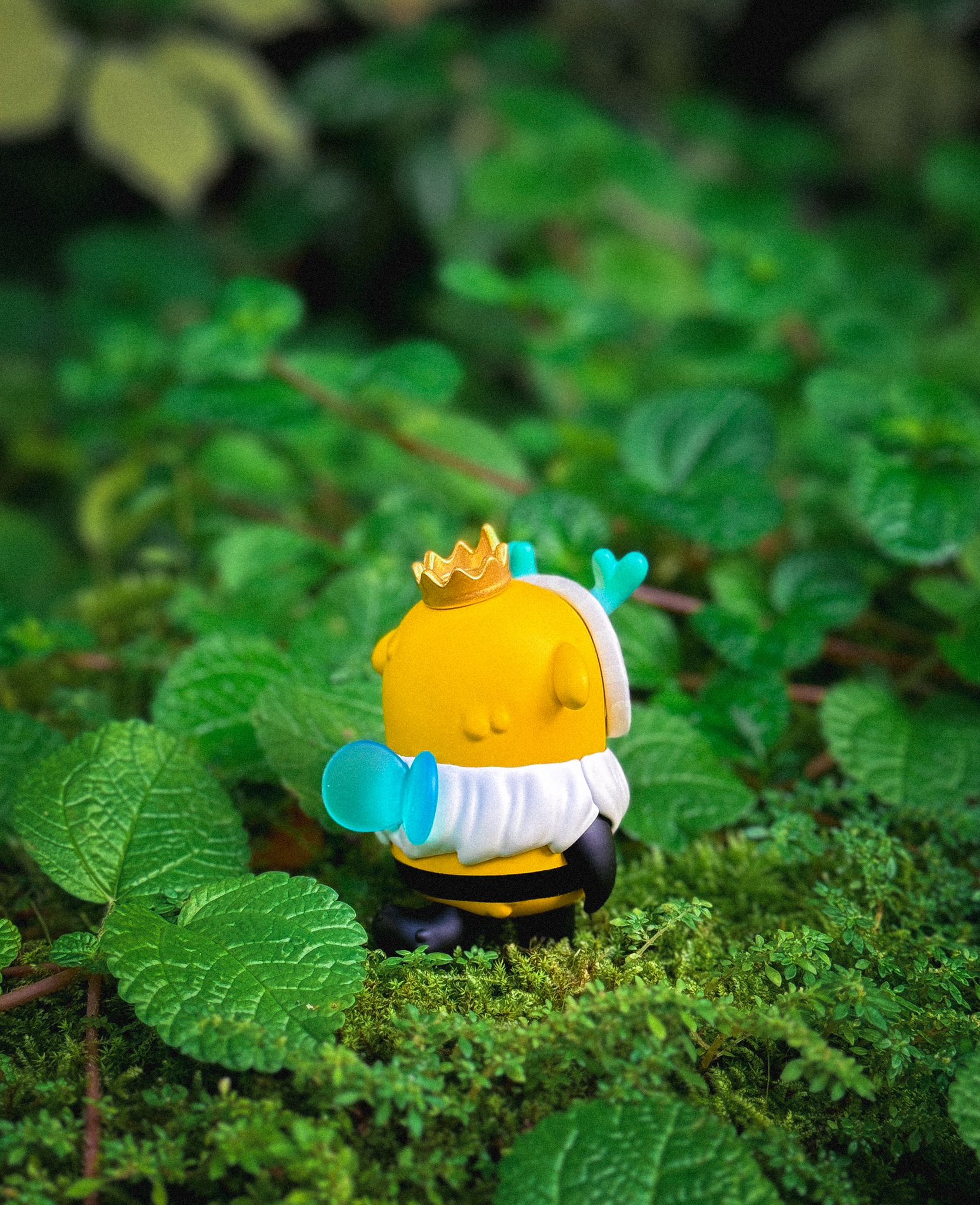 Little Muffinn: King Bee toy by Madkids, featuring a crown and blue pacifier, displayed outdoors on grass. Made of polyester resin, 6-7 cm tall.