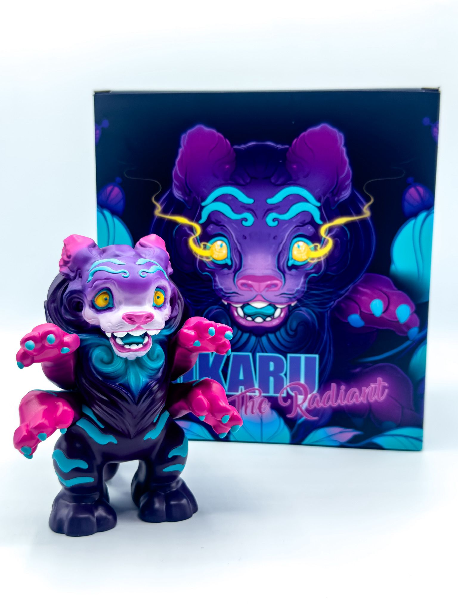 Hikaru - The Radiant by Tomodachi Island: A stylized feline vinyl figure with glowing eyes, UV reactive details, and a detachable tail, posed before its matching box.