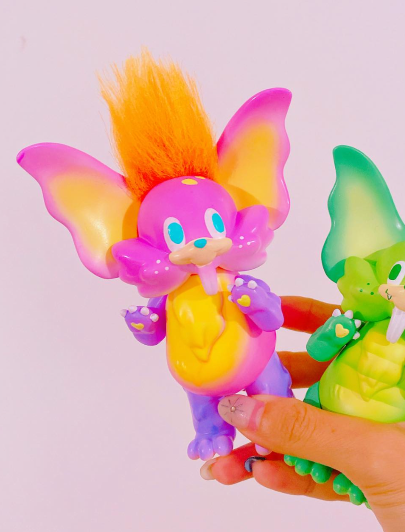 Hand holding two Little Bunny Dinosaur sofubi figures by Vivian Wang, featuring bat-like ears and fuzzy mohawks, showcasing vibrant collectible designer toys.