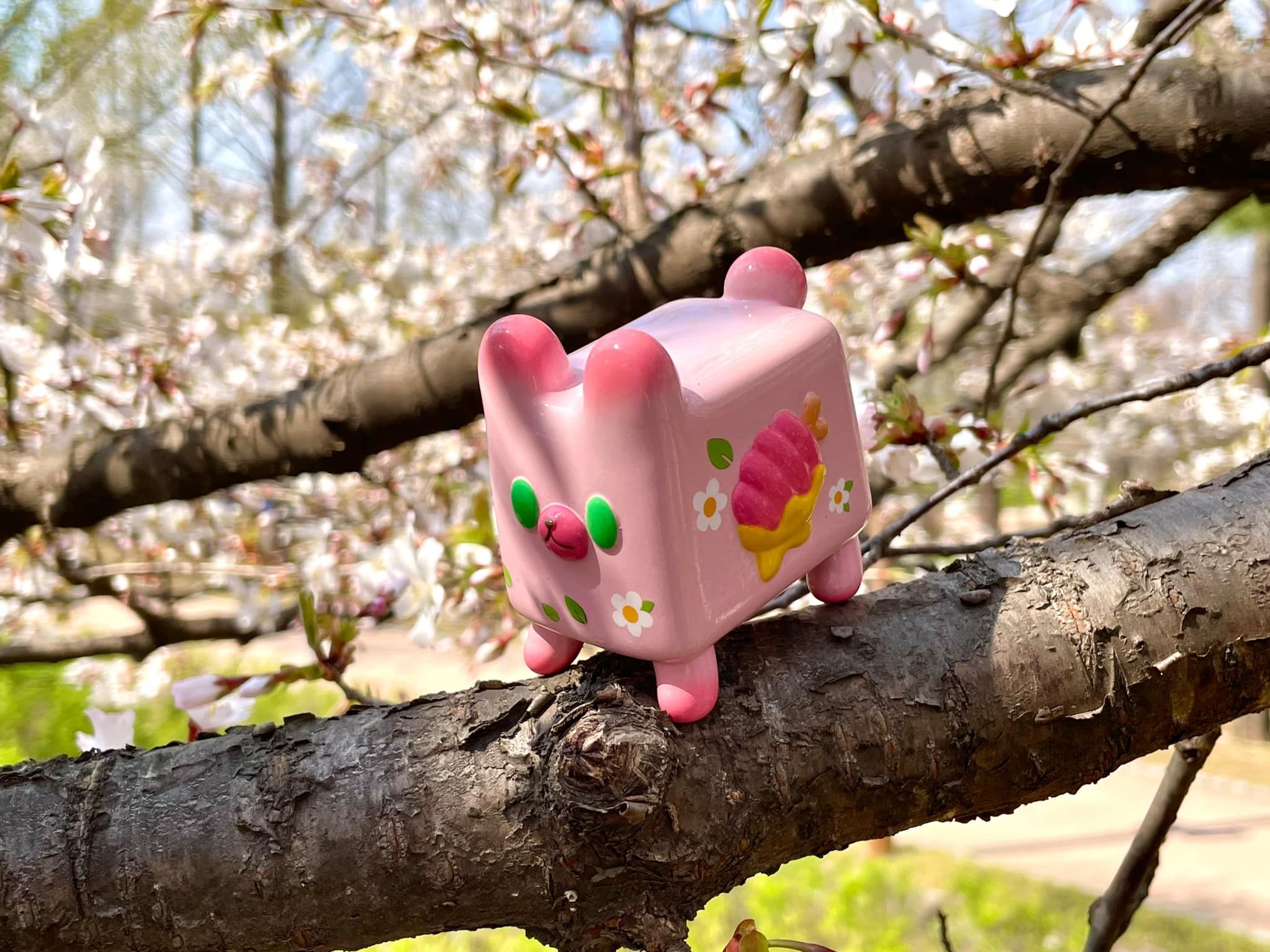 Box Bear - Sakura Spring Ver. by Rato Kim, a pink toy perched on a tree branch, showcasing its soft vinyl design, limited to 100 pieces.