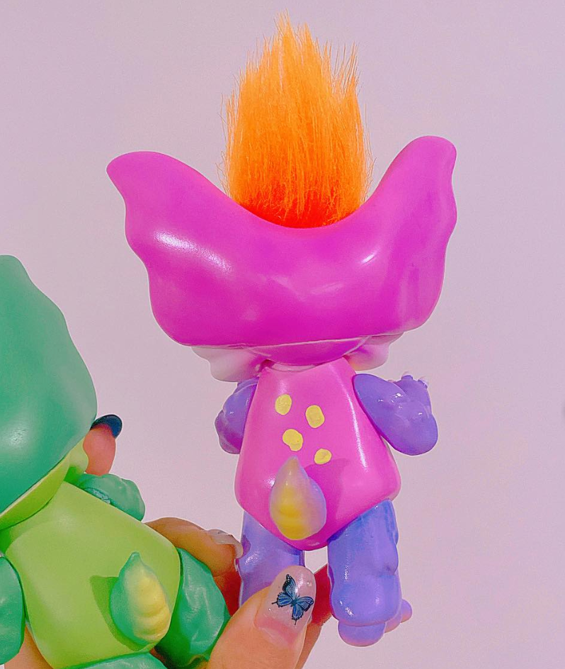 Two Little Bunny Dinosaur toy figurines by Vivian Wang, featuring oversized ears and fluffy hair, held in hand with a butterfly nail decal.