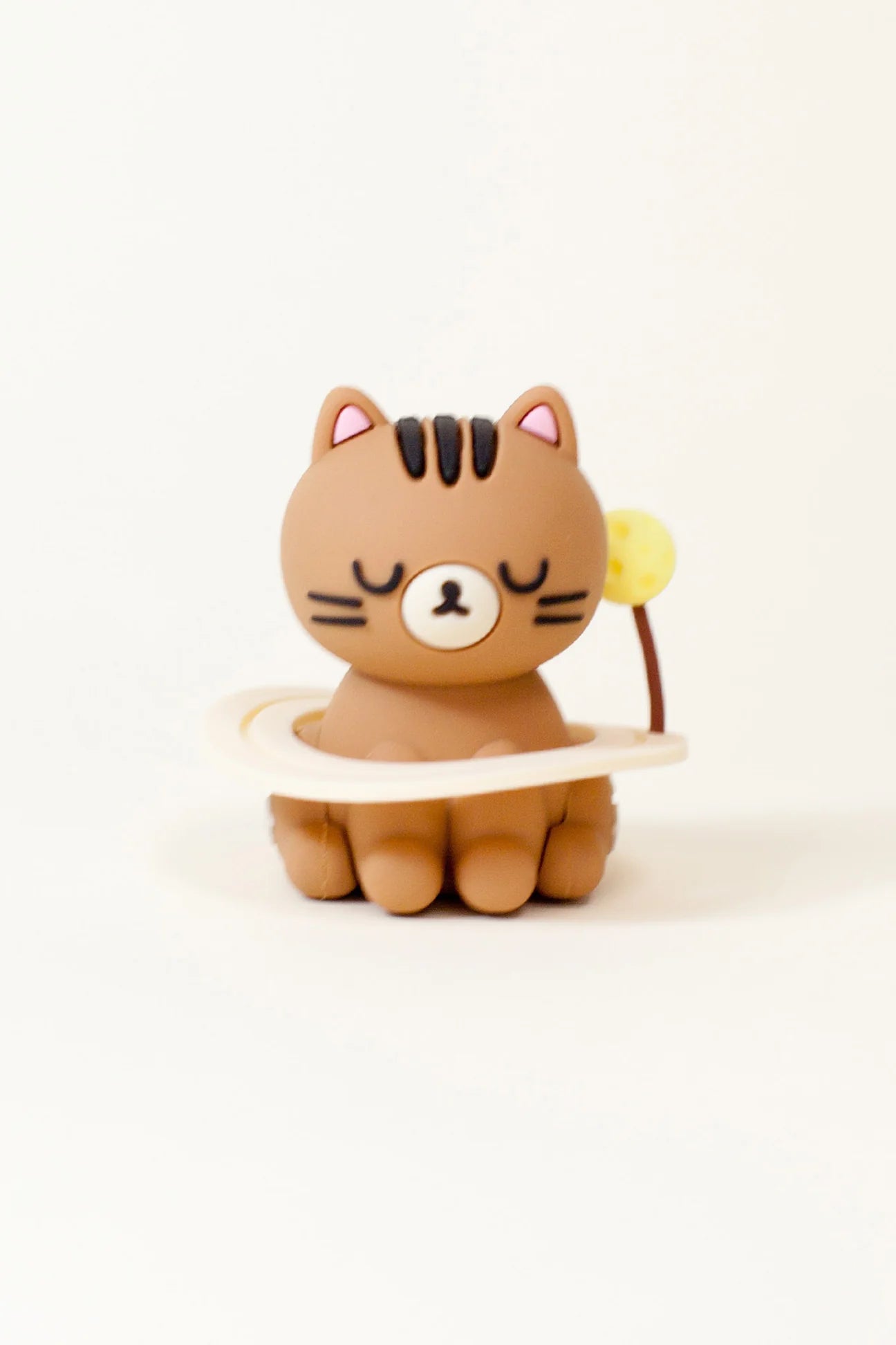Smoko Astro Cats Blind Box Figure: A light-brown, round-bodied cat figurine with closed eyes, black stripes, a cream ring, and a flower bud stalk.