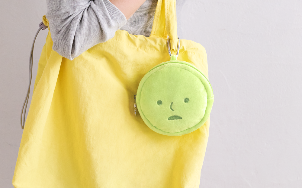 SMISKI Cushion Pouch attached to a yellow tote, featuring a minimalistic face. Perfect for carrying small items with a convenient carabiner clip. Preorder now.