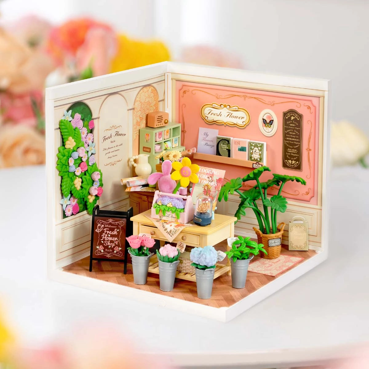 DW017B Fresh Flower Shop Rolife DIY Miniature House: a detailed dollhouse-scale florist scene with a worktable, potted flowers, chalkboard sign, and decorative elements.