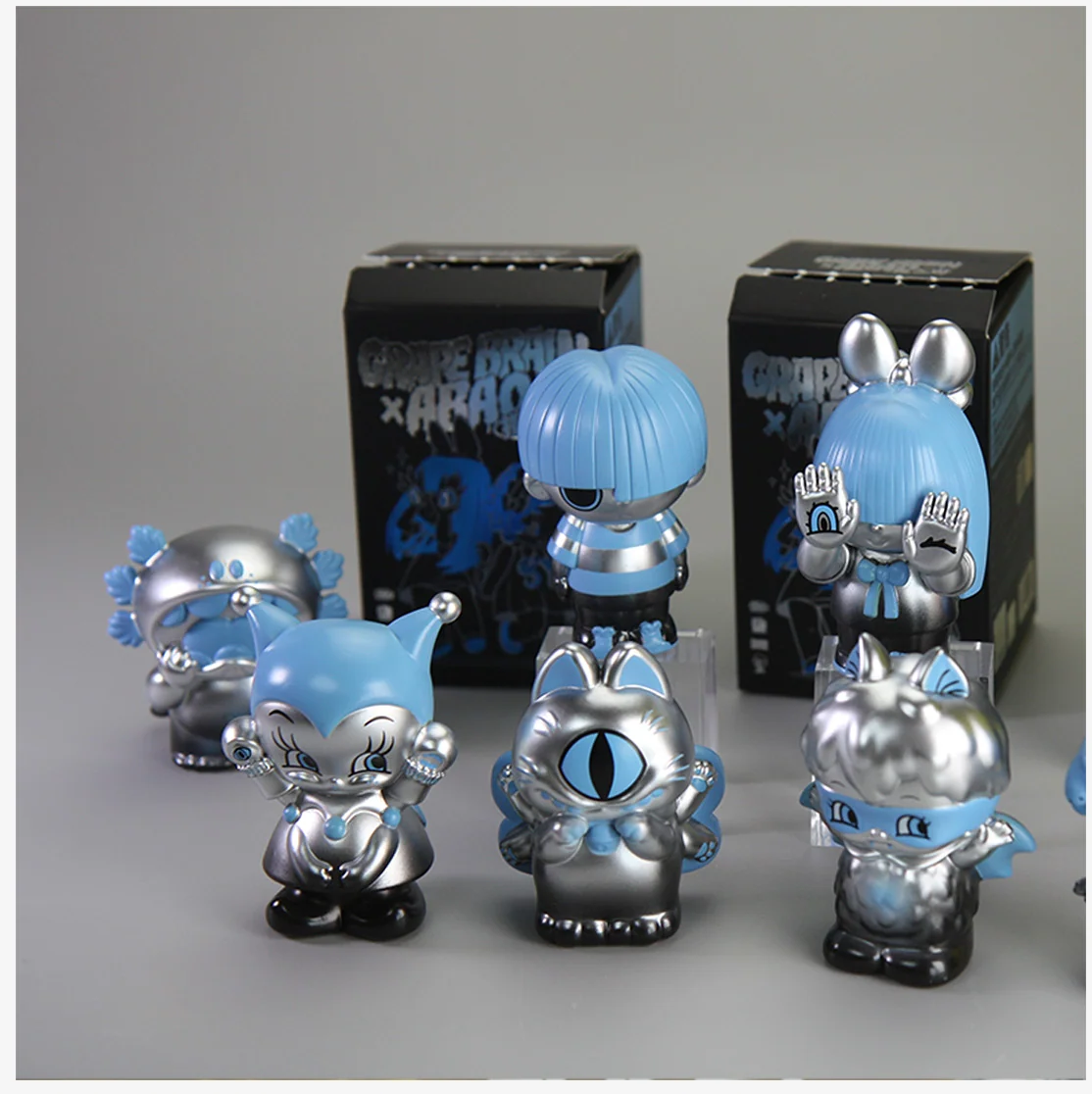 GRAPE BRAIN x ABAO BLINDBOX (SILVER AND BLUE) features six whimsical vinyl figures with metallic finishes, displayed in front of branded collaboration boxes.
