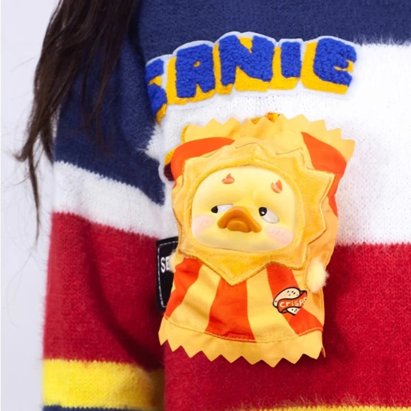 A person holds an Upset Duck - Pocket Crazy Circus Duck, a plush toy in a red-and-orange crisps costume with a pouty expression.