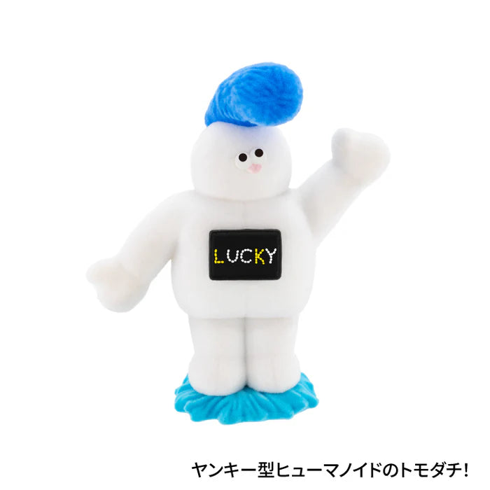 The TOMODACHI! Figure Collection Vol. 2 Gacha featuring a white humanoid toy with LUCKY on its chest, waving arm, and blue pom-pom tuft.