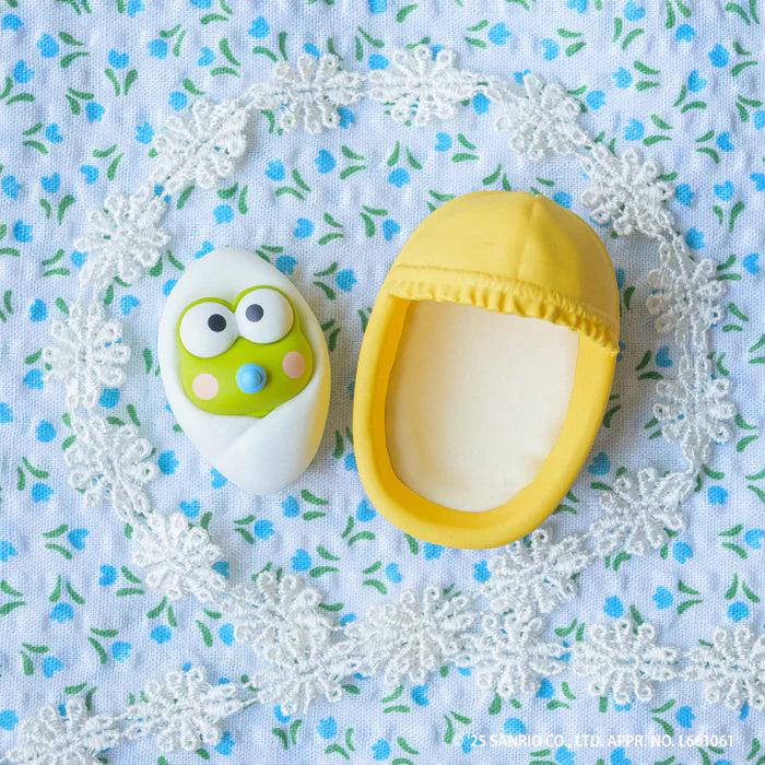 Sanrio Characters Baby Room Collection 2nd Edition Gacha Series: Keroppi figure in swaddle with yellow egg cradle, set on floral cloth.