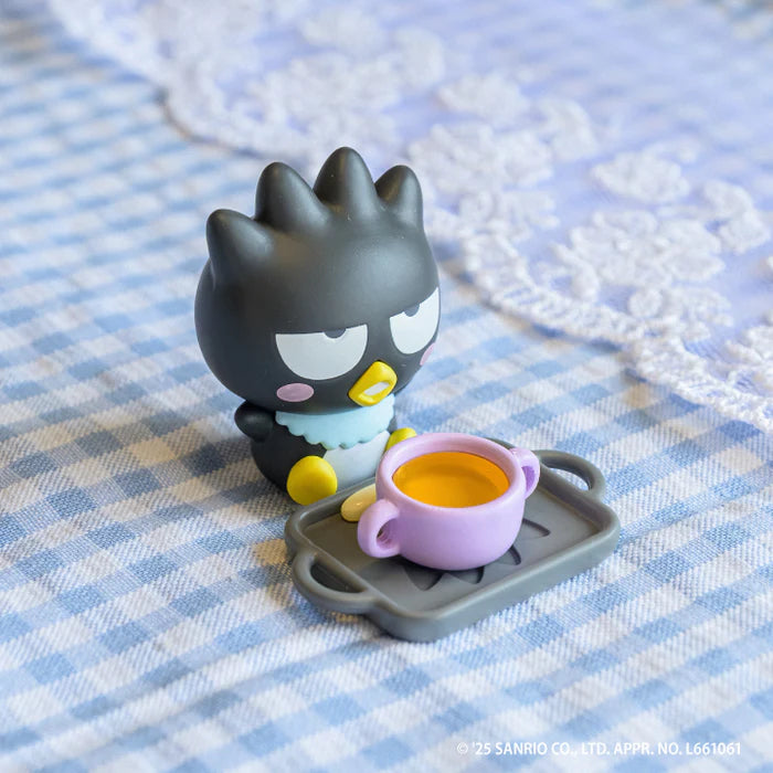 Sanrio Characters Baby Room Collection 2nd Edition Gacha Series featuring Badtz-Maru with accessories on a gingham cloth. A charming, collectible art toy scene.