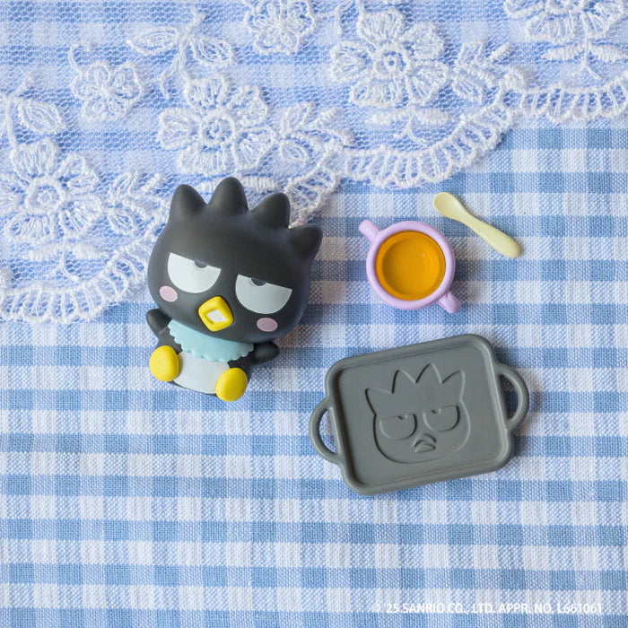 Sanrio Characters Baby Room Collection 2nd Edition Gacha Series featuring Badtz-Maru figure, cup, spoon, and tray on gingham cloth.