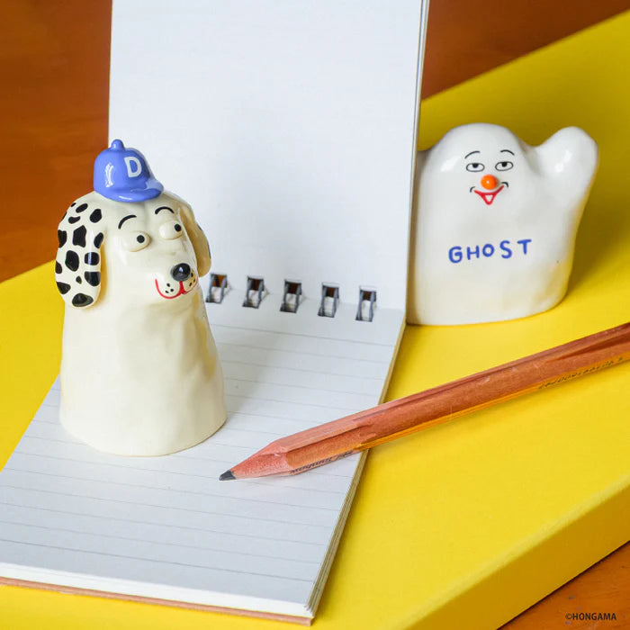 HONGAMA miniature collection Gacha Series featuring a spiral notepad, pencil, and ceramic figures: a dog with a D cap and a waving GHOST character.