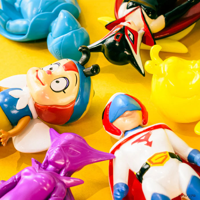 Tatsunoko Productions Characters Ball Chain Mascot Gacha Series featuring colorful figurines, including superheroes and creatures, laid out on a yellow surface.