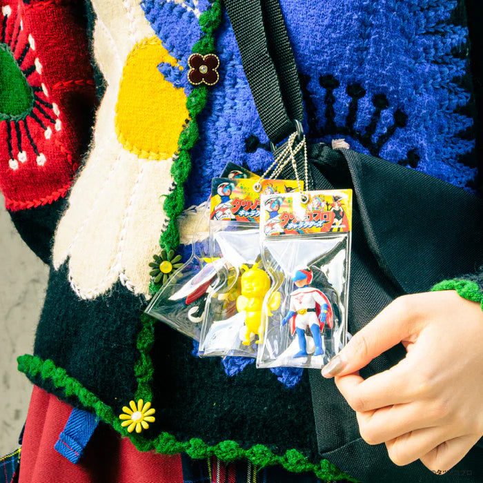 Hand holds three packaged Tatsunoko Productions Characters Ball Chain Mascot Gacha Series keychains, featuring a yellow mascot and red-and-white superhero figure.