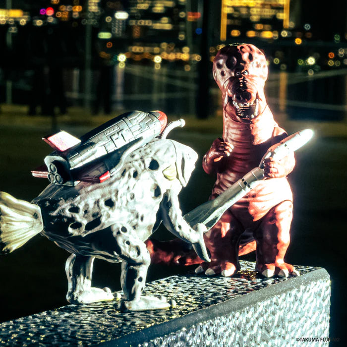 Takuma Fujisaki's 3D Monster Encyclopedia: Tokyo Monster Universe Vol. 2 Gacha features stylized monster toys engaged in a playful duel with city lights in the background.