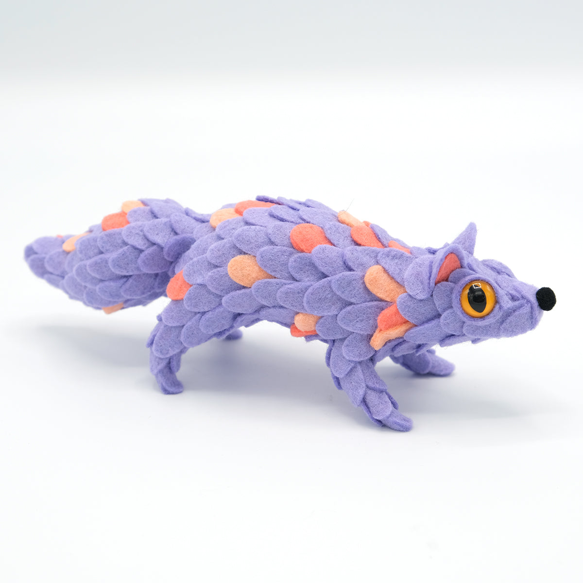 Whimsical lavender plush toy resembling a fox-pangolin hybrid, featuring layered scales and one visible yellow-orange eye. Part of ORACLE Group Show by Horrible Adorables x Faunwood.
