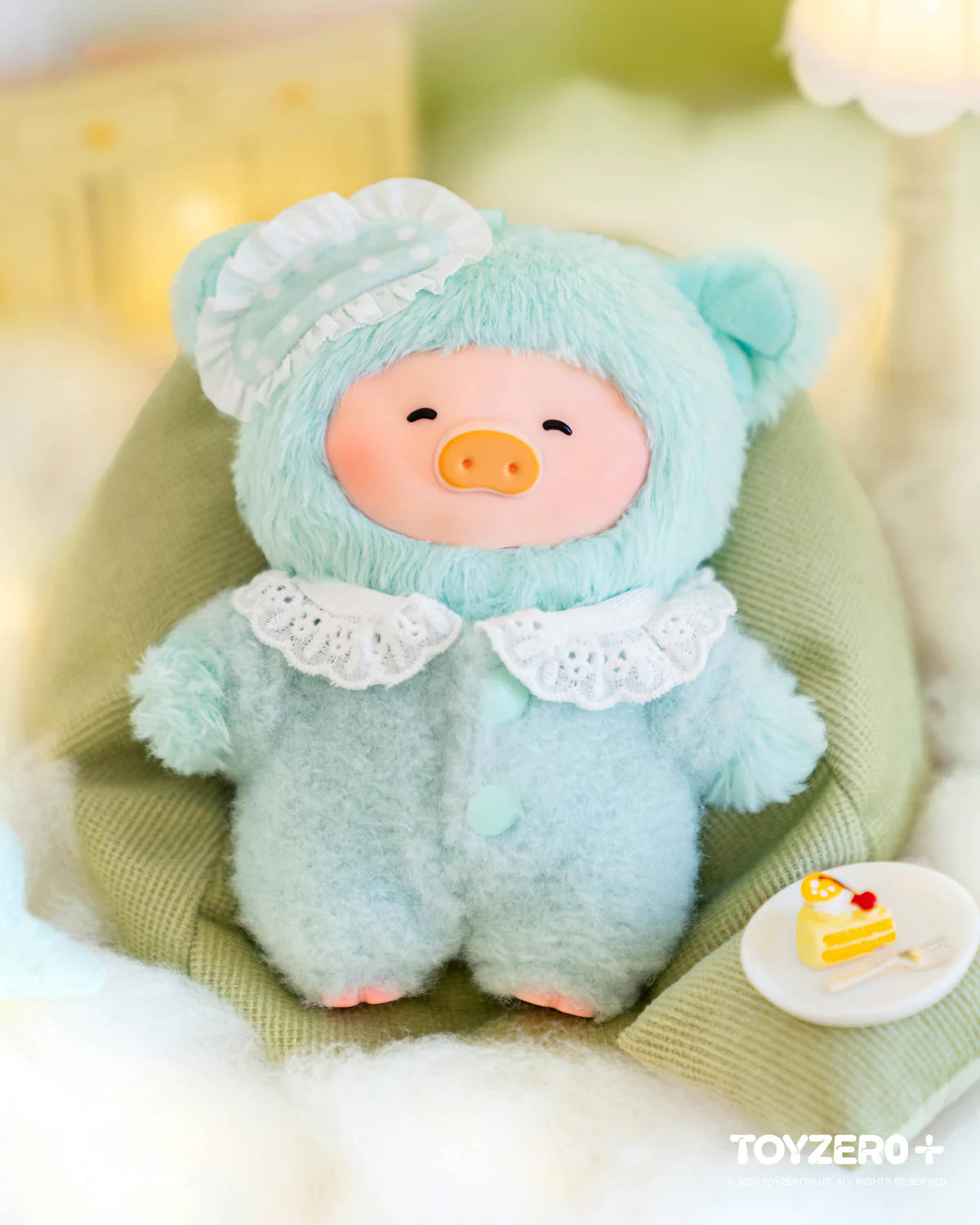 LuLu the Piggy plush in a mint bear onesie with bonnet, sits on a cushion beside a toy cake. Part of LuLu's Dreaming Wonderland Series Blindbox.