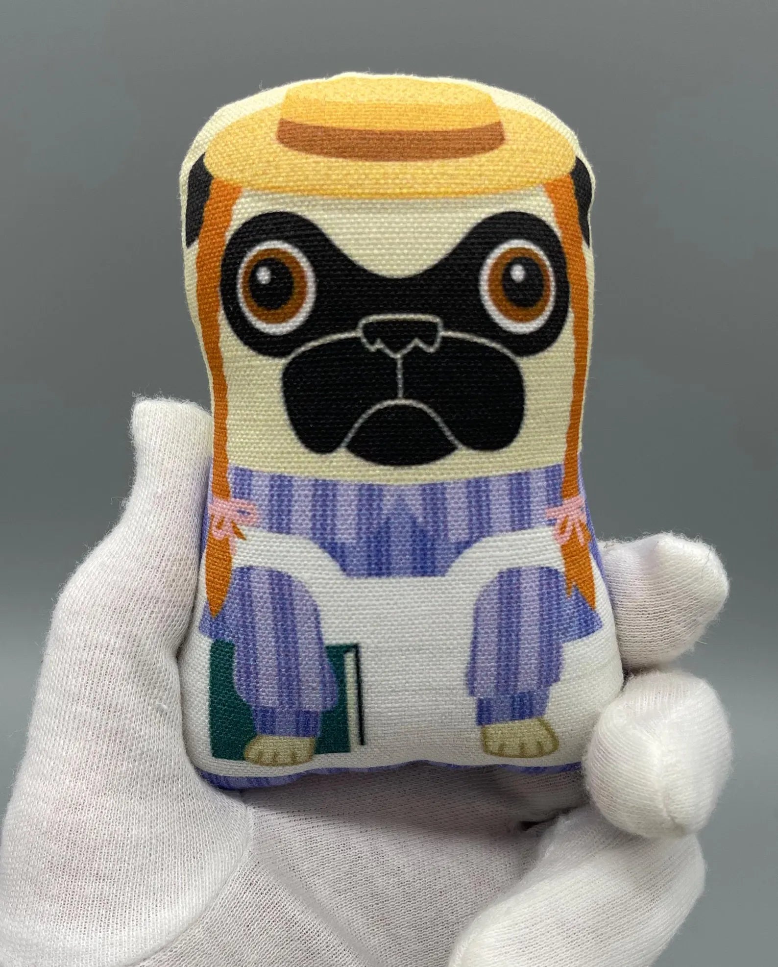 Nerfect Pug Surprise / Series 12: Close-up of a hand holding a pocket-sized, blind-bagged plush toy, featuring handcrafted details and unique pug character design.