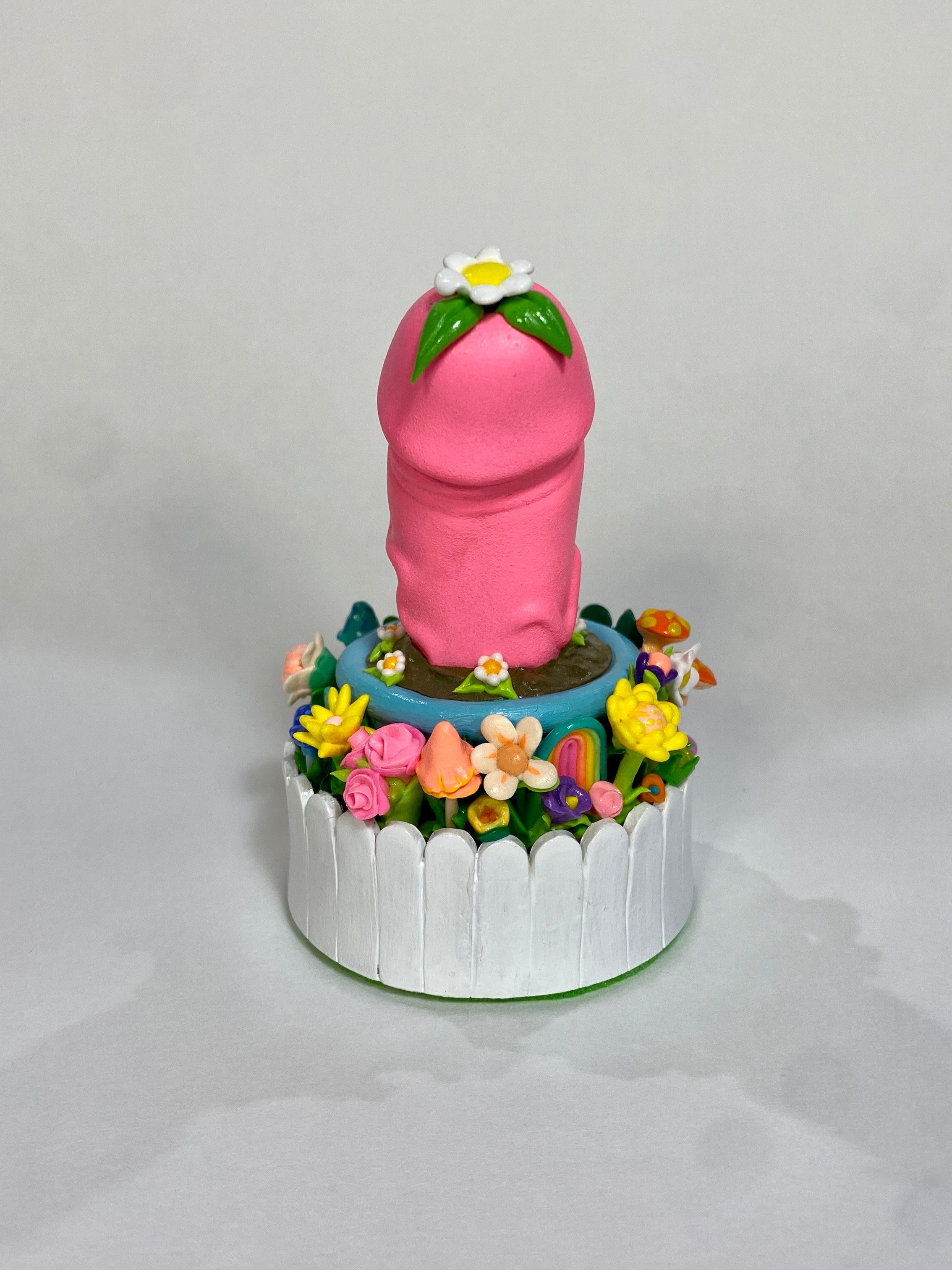 Sculpture of a hand holding a glove with a pink toy, flowers, and a cake in the image.