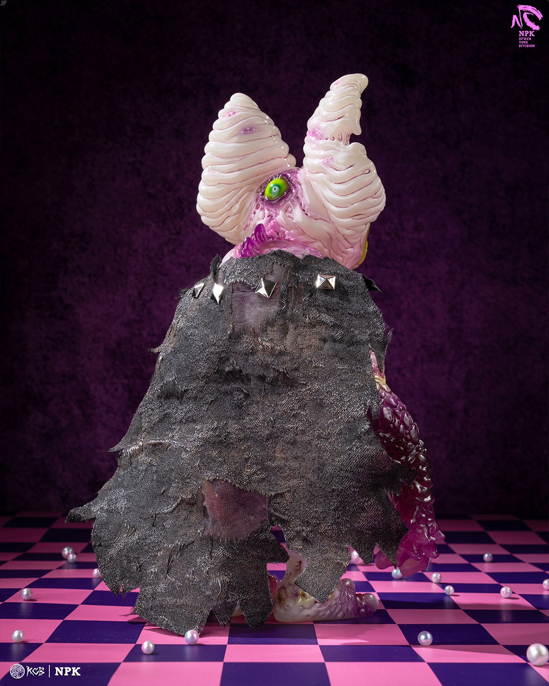 Stylized vinyl figure NPK · Poison Veil Ver. with a horned, one-eyed design in a black cape, posed on a checkerboard floor. Preorder for Strangecat Toys.