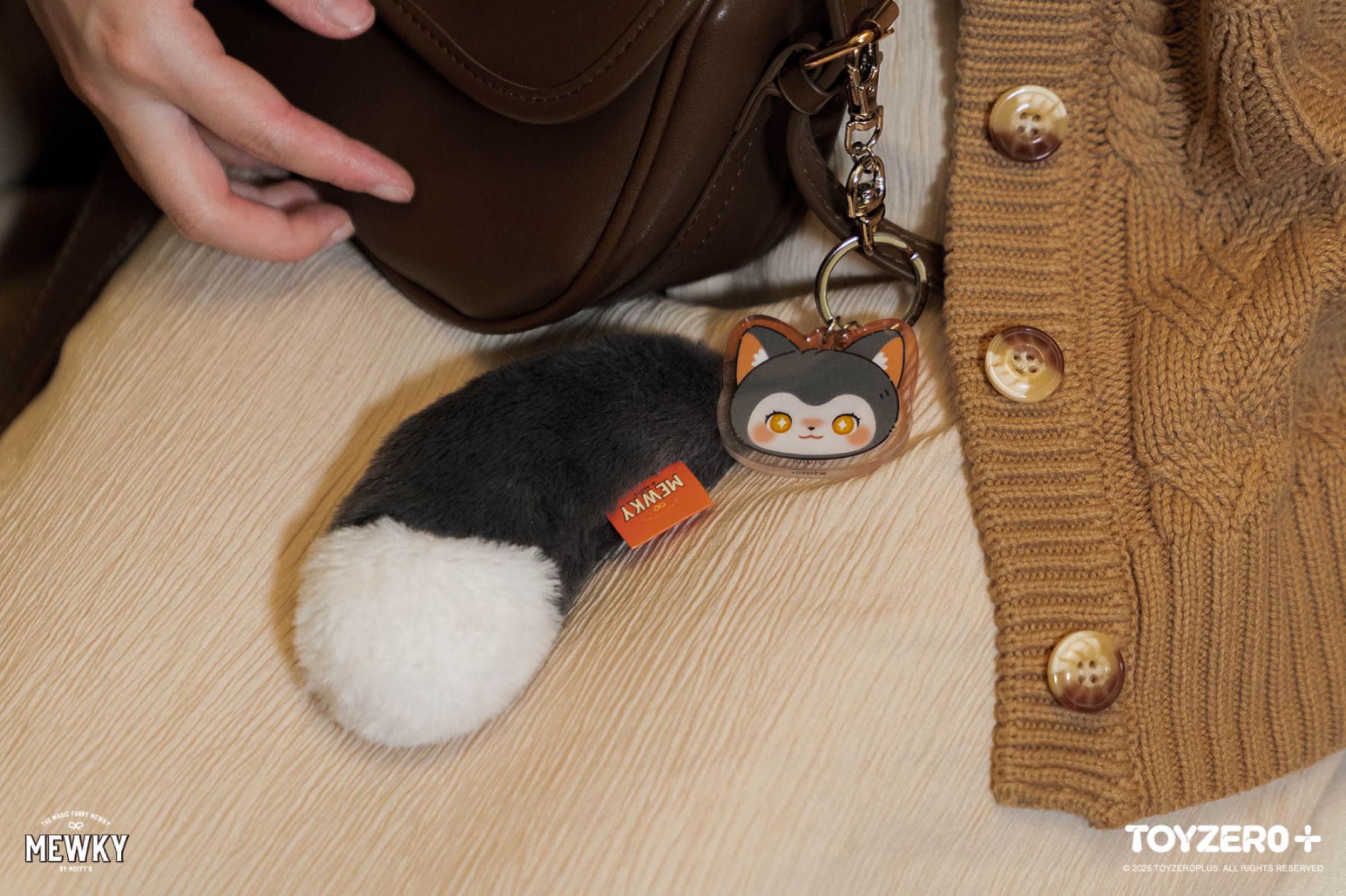 Moffy's - Mewky Cat Tail Keychain - Black Cat clipped to brown leather purse beside a cable-knit cardigan, featuring a stylized cat face charm.
