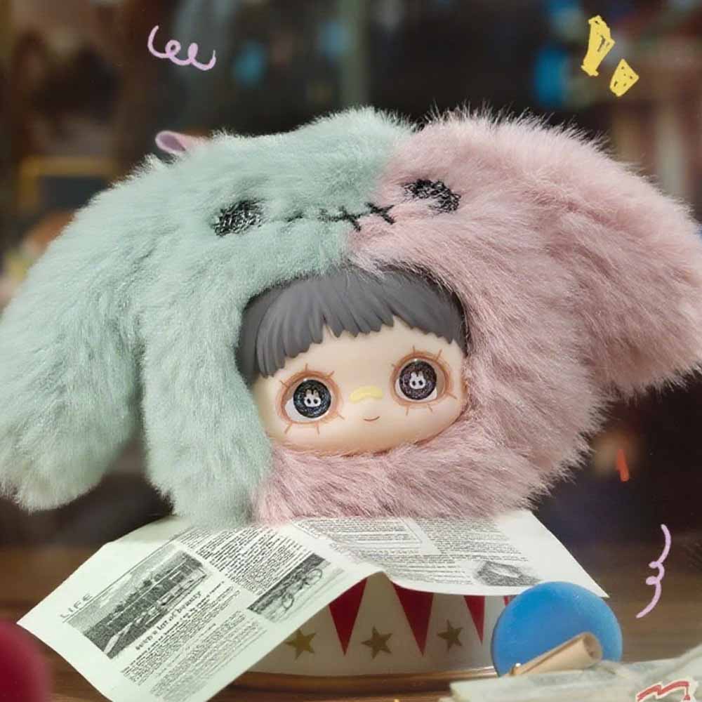 MayMei Crazy Circus Series Plush Keychain Blind Box featuring a doll with a bunny-ear hood, sitting on a circus-themed box with doodles around.