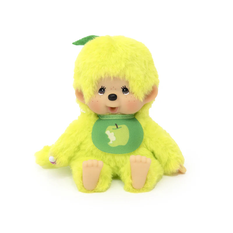 Monchhichi Fruit Beanies Plush with big eyes and freckled cheeks, dressed in green fur with an apple-themed bib, seated with visible plastic feet and hands.