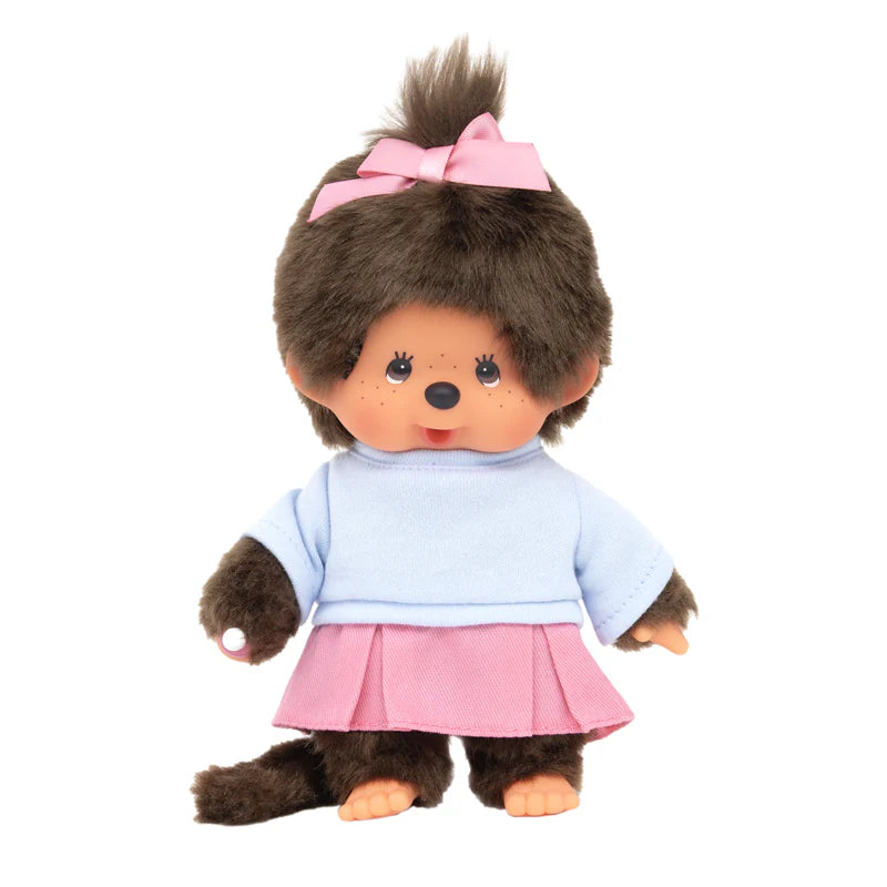 Monchhichi Skirt Girl Plush: round-faced doll with big eyes, brown faux fur, pink skirt, blue top, pink bow, and thumb-sucking feature. Perfect for collectors.
