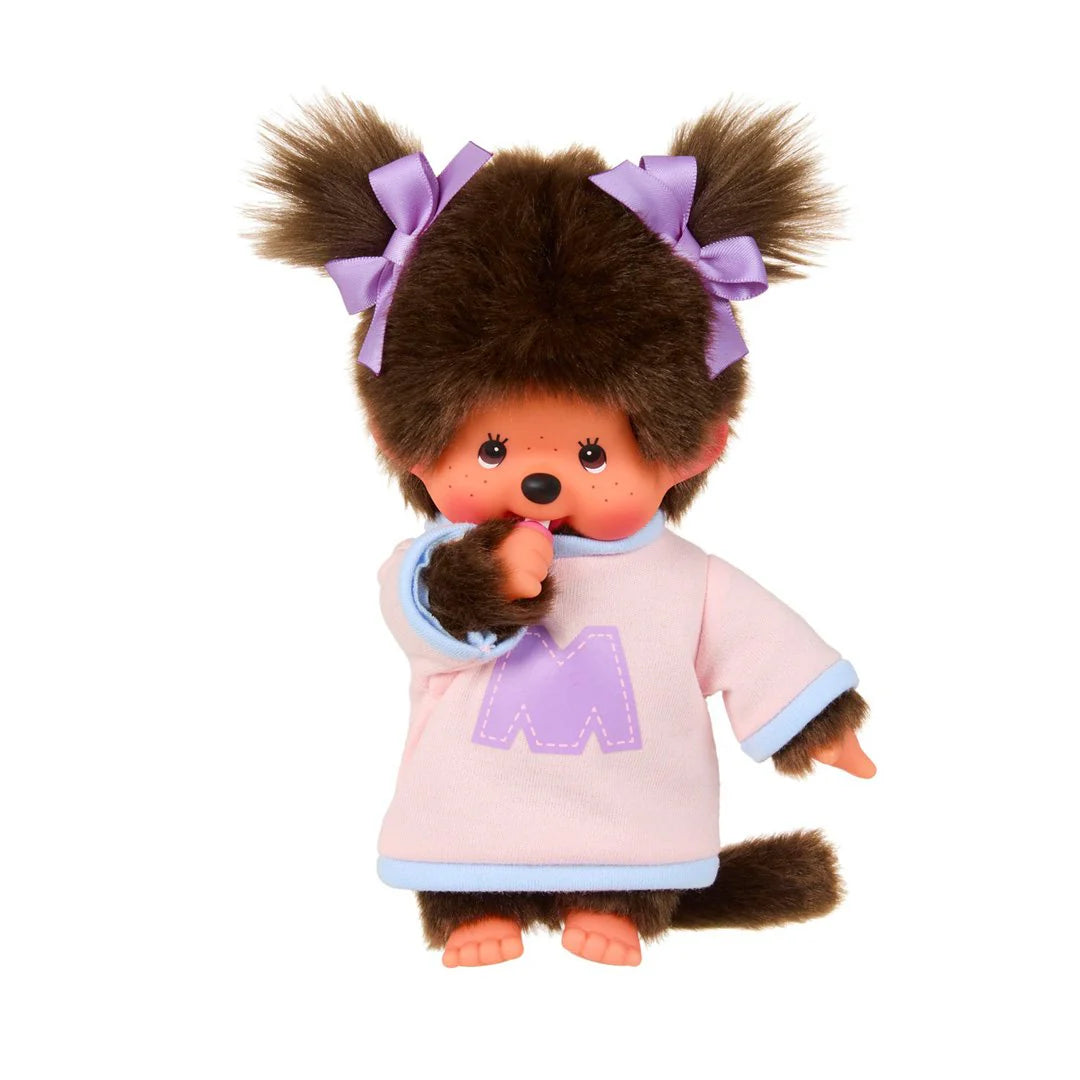 Monchhichi Girl - Bi-Colored Sweater Plush Toy with pigtails, lavender bows, and thumb-sucking pose, wearing a pink tunic with purple “M”, embodying cozy charm.