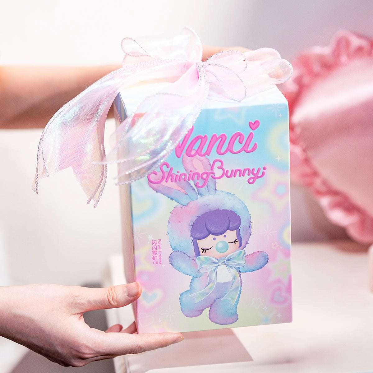 Hand holding Nanci's Shining Bunny Plush Blind Box, featuring a pink fabric bow, showcasing Strangecat Toys' surprise art toy collection.