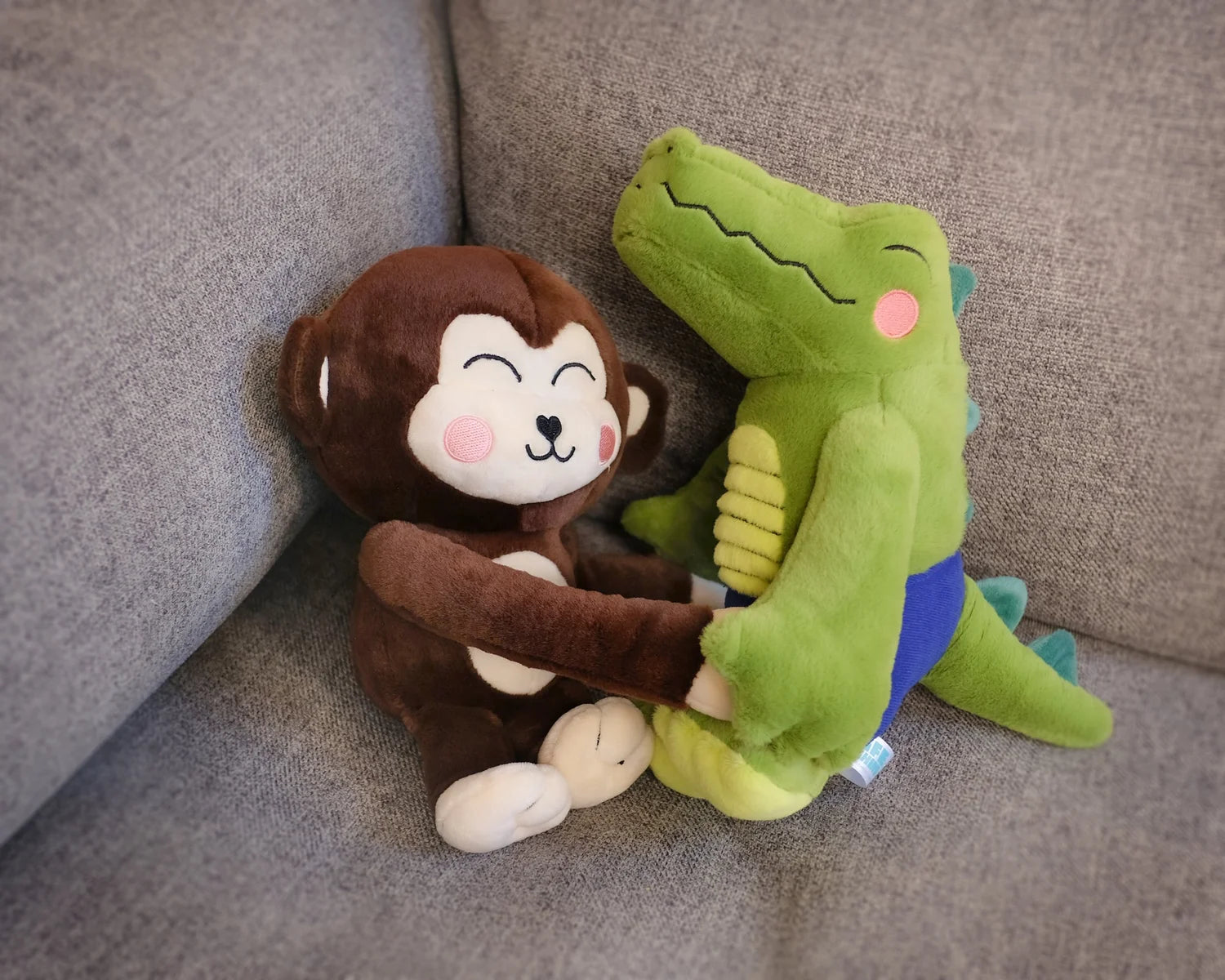 Monkay + Alligator Plush by Life Machine: Two plush toys hugging on a grey couch, featuring magnetic accessories for harmonious play.