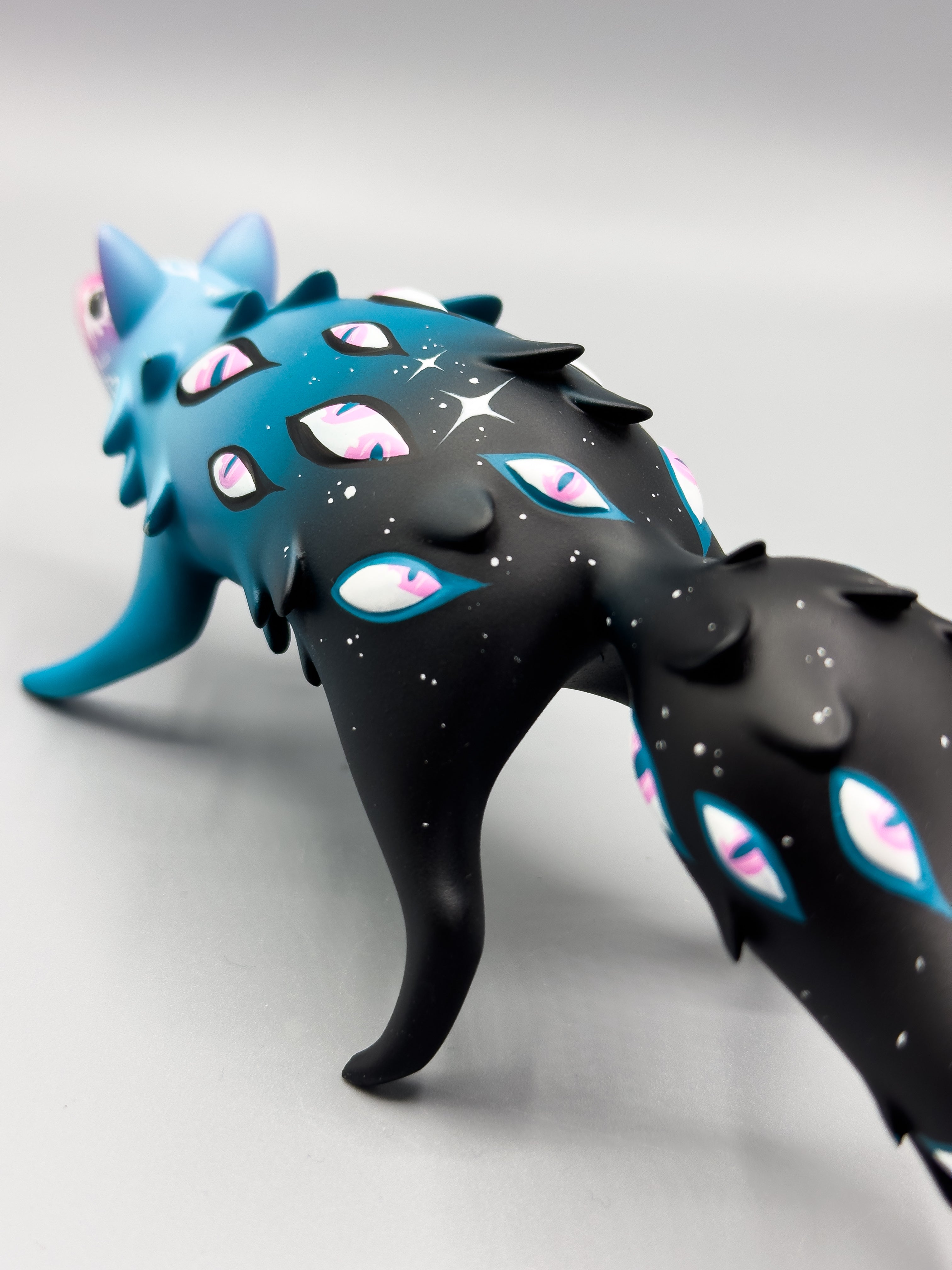Cosmyrr by Tomodachi Island x Faunwood: 10cm resin figurine, featuring teal-blue to black gradient, eye motifs, and star specks, showcased for ORACLE Group Show.