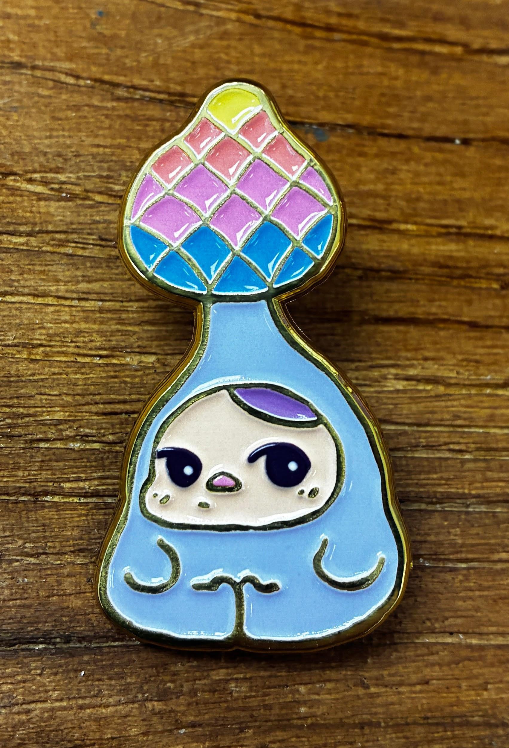 Bloom Pins by Pucky: A colorful enamel pin featuring a mosaic spade design with a shy cartoon creature in a blue suit on a wooden surface.