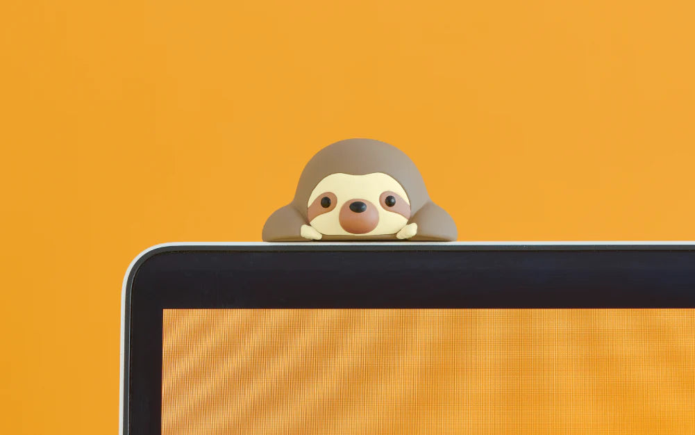 HIPPERS Funbarus (Posture Pal) sloth figurine peeks over a laptop screen, serving as a decorative webcam cover or fun screen topper.