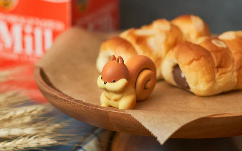 Animal Bakery Minifigure: Series 2 featuring a cinnamon roll squirrel figurine displayed on a plate of pastries, representing the playful and surprising blind box art toys.