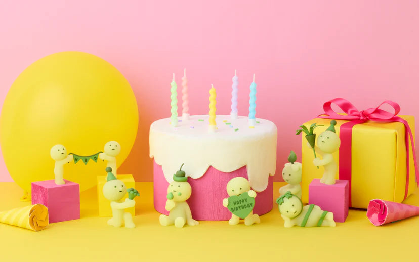 SMISKI Birthday Series figurines surround a two-tone cake with pastel candles, alongside a balloon, gift box, and party horns for a whimsical celebration scene.