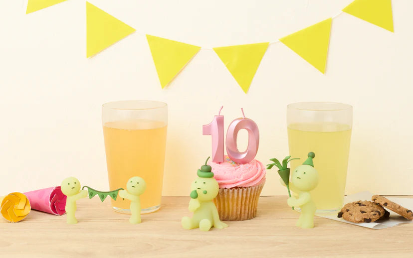 SMISKI Birthday Series celebration setup with figurines, pink “10” candle on cupcake, cookies, party blower, and juice, reflecting a playful 10th anniversary theme.