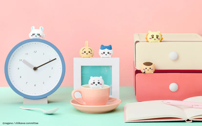 HIPPERS CHiiKAWA mini figures adorning a desktop, perched on a clock, teacup, photo frame, and pastel cabinet, enhancing everyday items with cuteness.
