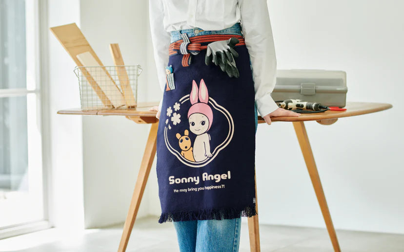 Sonny Angel x Anything Maekake Apron showcased with tools; features a bunny graphic and supports artisanal work, blending traditional style with modern DIY practicality.