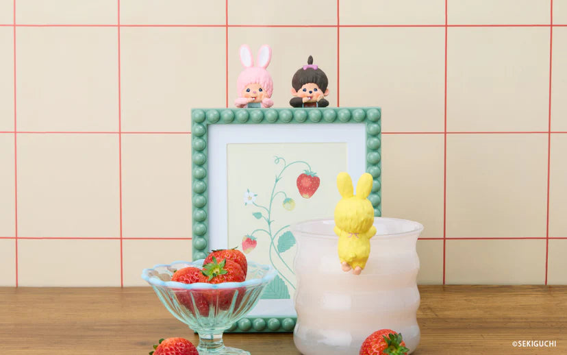 Monchhichi HIPPERS figures adorn a mint-green frame with strawberry illustration, surrounded by strawberries and a frosted tumbler, highlighting their decorative versatility.
